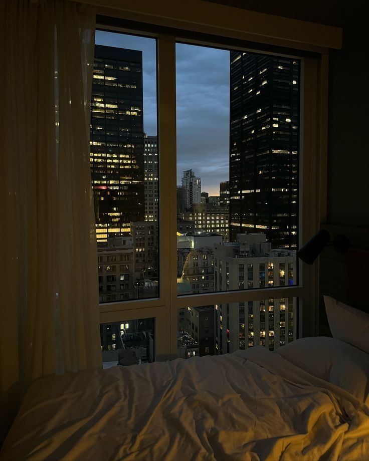Nighttime bedroom with large window overlooking illuminated city skyline