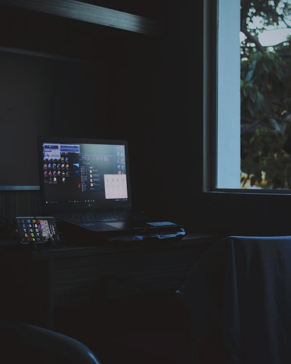 A Laptop and a Mobile Phone on the Wooden Table in a Dark Room